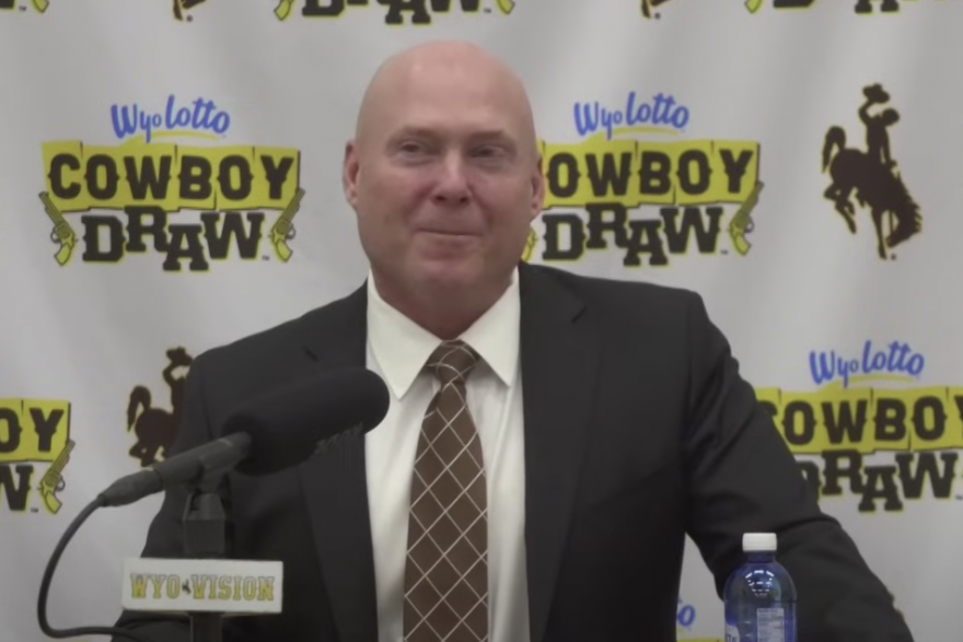 Jay Sawvel, the new head coach of the University of Wyoming football team, stands at a podium addresses the media while wearing a suit.