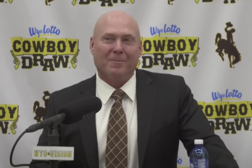 Jay Sawvel, the new head coach of the University of Wyoming football team, stands at a podium addresses the media while wearing a suit. 