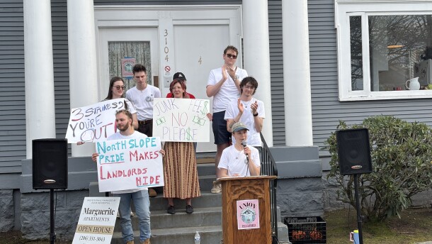 People holding signs stand outside a gray building with columns. 