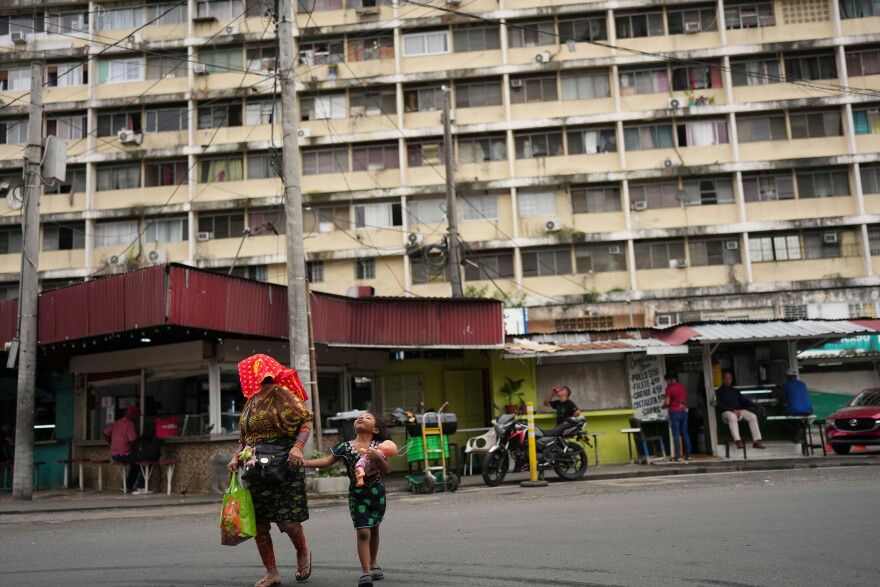 A woman and a child cross a street, with a residential high rise behind them. 