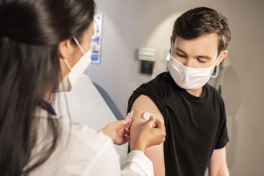  In this 2020 photograph, captured inside a clinical setting, a health care provider places a bandage on the injection site of a patient, who just received an influenza vaccine. The best way to prevent seasonal flu, is to get vaccinated every year. Centers for Disease Control and Prevention (CDC) recommends everyone 6-months of age and older get a flu vaccine every season.