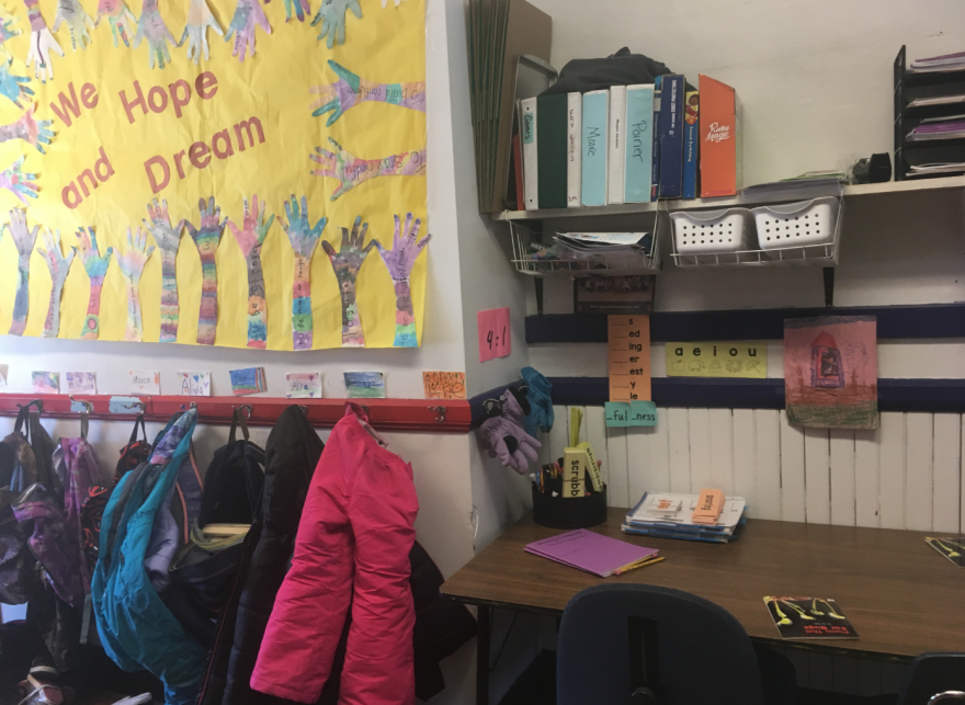 A bulletin board at a school reads "We Hope and Dream," surrounded by coats and backpacks.