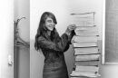 woman stands beside a stack of papers