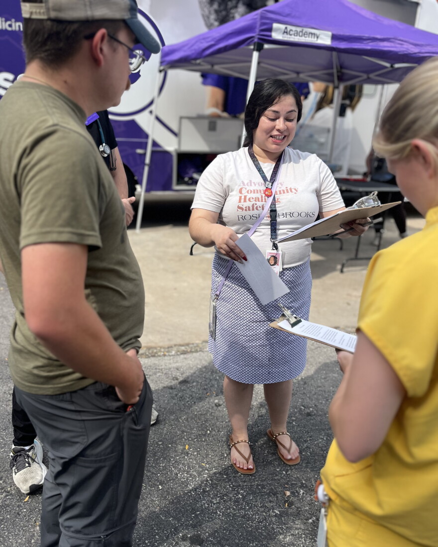 A women with dark hair, a white shirt and a blue skirt talks to a group of student veterinarians from Kansas State University. 