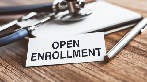 The text open enrollment is written on notepad near a stethoscope on a wooden background. Medical concept