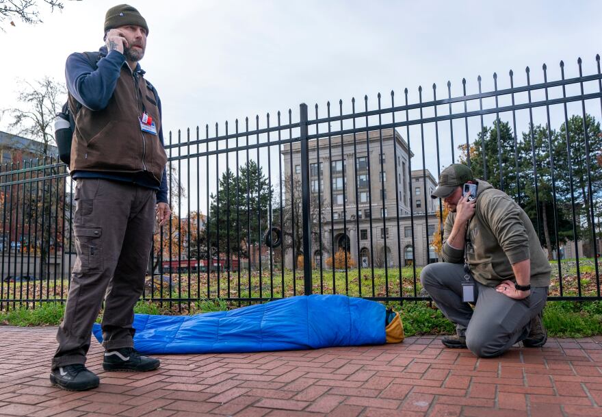 Outreach worker Ryan Hazlett, with Mental Health & Addiction Association of Oregon, and a representative from Recovery Works NW, right, make calls to find treatment options for a man sick from fentanyl, center, in downtown Portland, Ore. on Dec. 13, 2023. The work was part of a pilot program by Portland Police Bureau’s bike squad and addiction recovery providers that launched in December 2023.