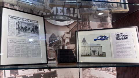 A lit glass case depicts a newspaper article, photographs and old meeting-minute books from the Village of Amelia.