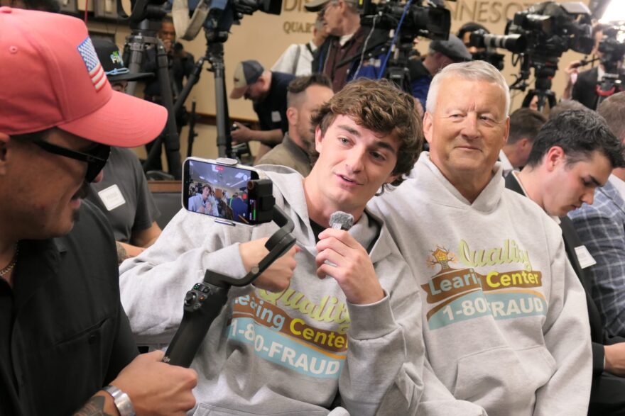 Right-wing influencer Nick Shirley and Republican activist David Hoch, who posted viral videos about alleged fraud by child care providers in Minnesota, film a video before Trump administration officials announce 15 indictments for Medicaid fraud in Minneapolis on May 21, 2026.