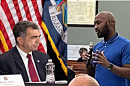New York State Assembly member Bill Magnarelli seated at a microphone and Onondaga County Legislator Maurice Brown standing in a meeting with a microphone
