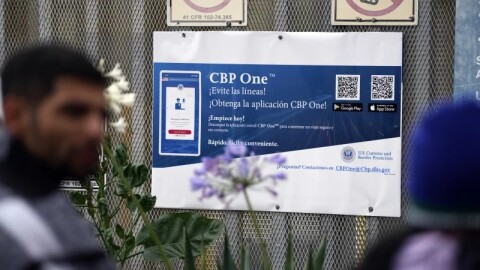 People waiting to apply for asylum stand in front of a sign for the CBP One app as they camp near the pedestrian entrance to the San Isidro Port of Entry, linking Tijuana, Mexico with San Diego.