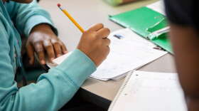 A student writes with a pencil at a table.