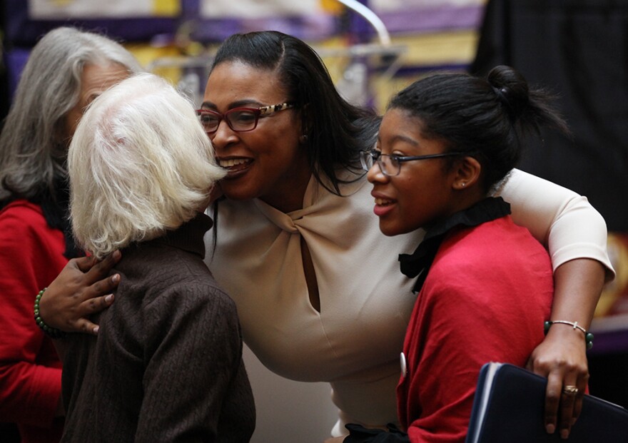 Mayor Lovely Warren hugs a woman attending the City Hall announcement of Rochester's suffrage centennial celebration events while 14-year-old Mariedeliz Bain of Rochester, portraying Susan B. Anthony, looks on.