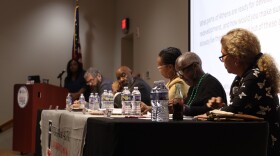 Candidates sit at a table with a projected question displayed on a screen behind them.