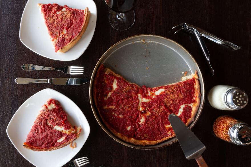 A Chicago-style pizza on a platter, next to slices of pizza on white plates. 