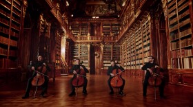 Four cellists sit in a line, in an ornate baroque library