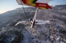 A hang gliding pilot flys over a snow covered mountain