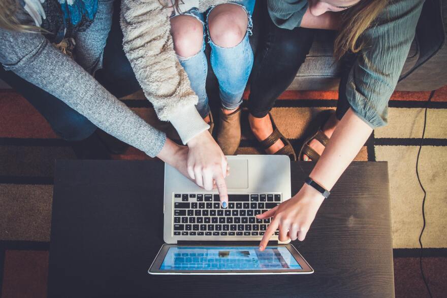 A group of people look and point at a laptop screen.