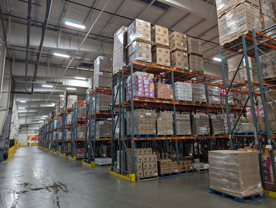 Stacks and pallets of boxes line rows in a giant warehouse. The boxes contain food supplies and reside in a Harvesters warehouse.