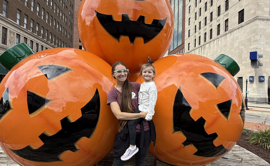 A woman stands with a child in front of large jack-o-lantern ornaments