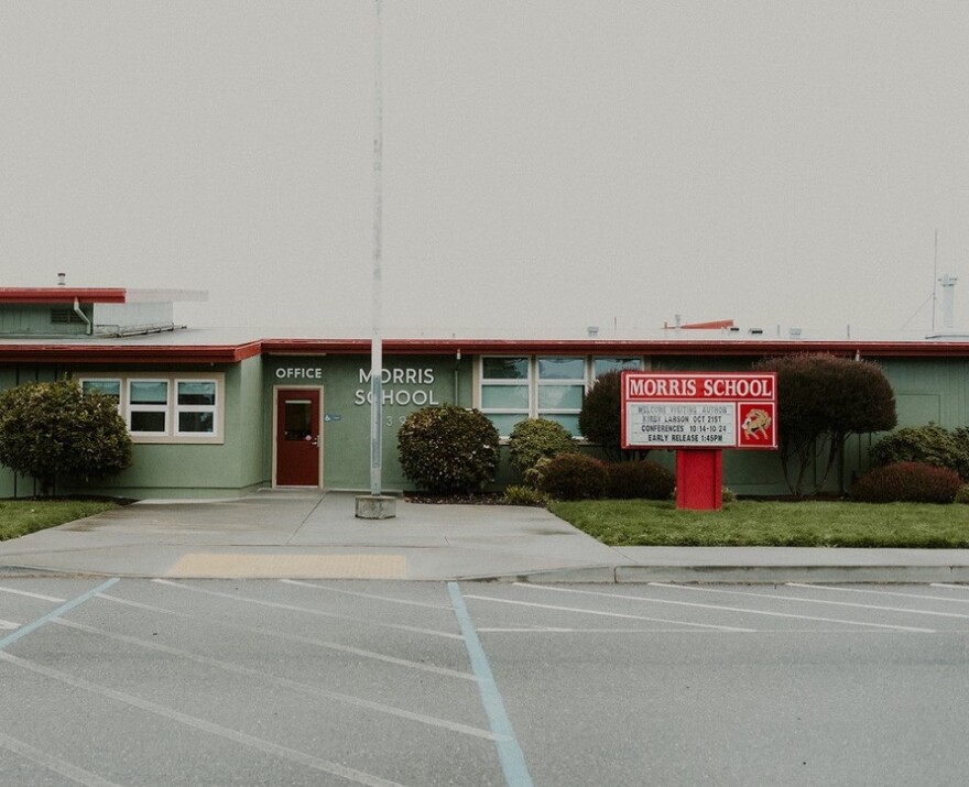 A single-story green school building, with grass and a flagpole in front. 