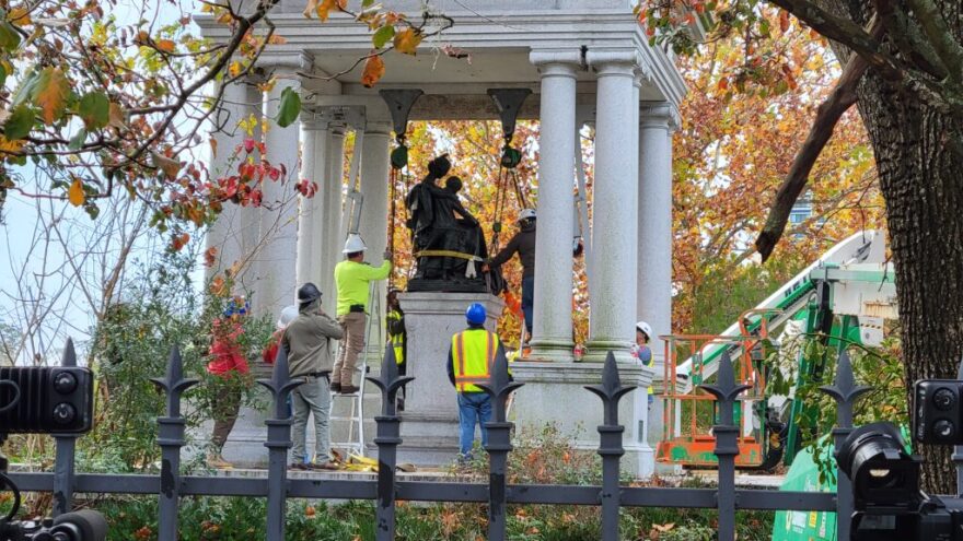 Workers secure straps around a statue.