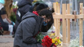 Star Samkus, who works at a King Soopers grocery store in Boulder, Colo., and knew three of the victims of a mass shooting there a day earlier, kneels in front of crosses put up for the victims outside the store on Tuesday.