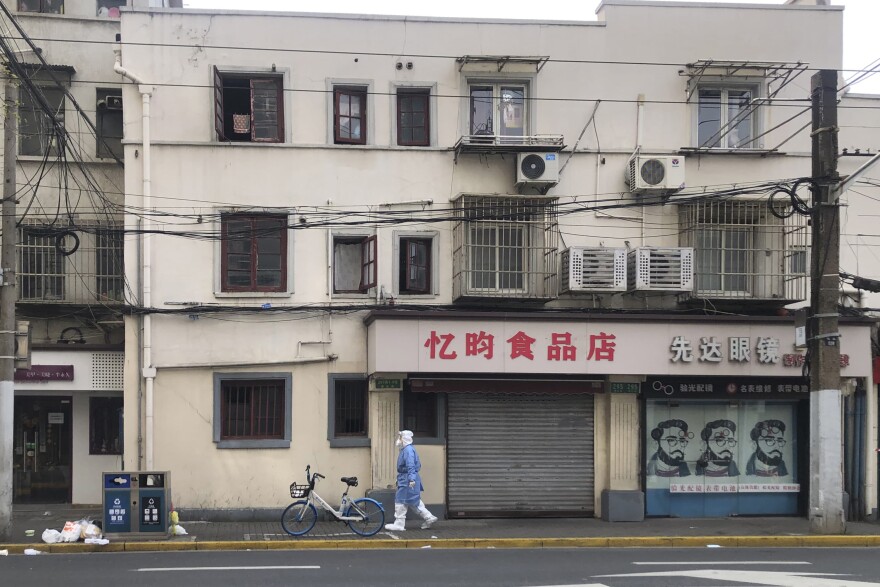 A worker in protective gear walks along shuttered shops in the Jingan district under lockdown in western Shanghai, China, Friday, April 1, 2022. (Chen Si/AP)