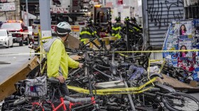 A biker stops to look at a pile of e-bikes in the aftermath of a fire in Chinatown, which authorities say started at an e-bike shop and spread to upper-floor apartments, Tuesday June 20, 2023, in New York. Federal officials are looking into cracking down on defective lithium-ion batteries that power hoverboards, scooters and motorized bicycles because of a rash of deadly fires caused by exploding batteries. 