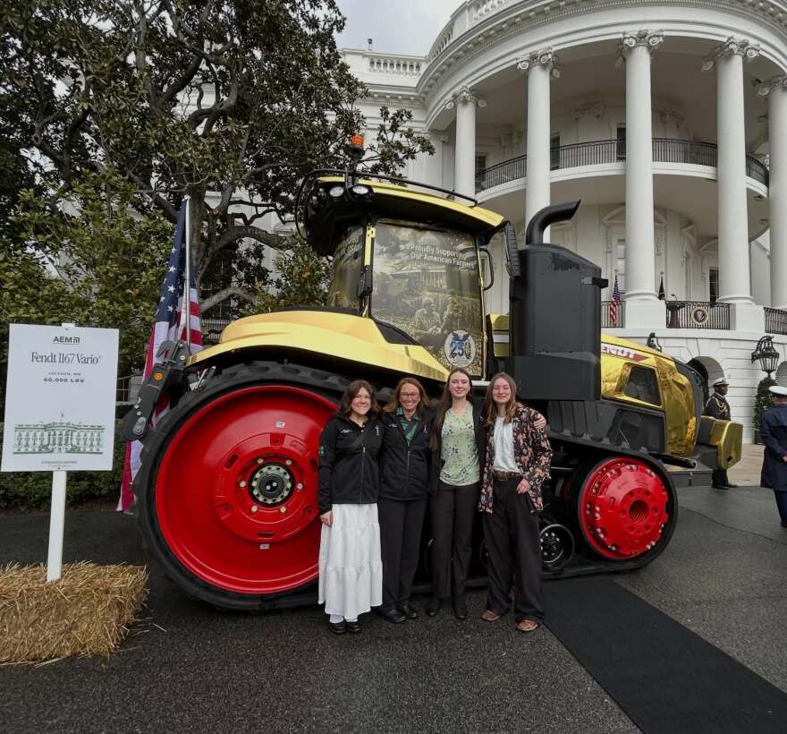 Four women standing in front of a gold-painted tractor in front of the Whitehouse.