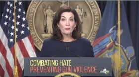 Gov. Kathy Hochul stands at a podium that says, "COMBATING HATE PREVENTING GUN VIOLENCE," in front of the state seal and between a U.S. and state flag.