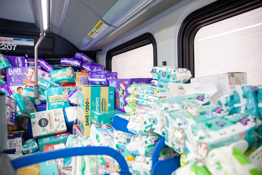 A bus interior filled with stacked boxes and packages of diapers in various brands and sizes, covering the seats and windows.