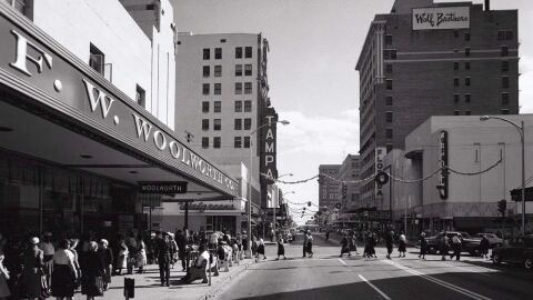A vintage black/white photo showing F.W. Woolworth to the left with a street in the middle and tall buildings in the background