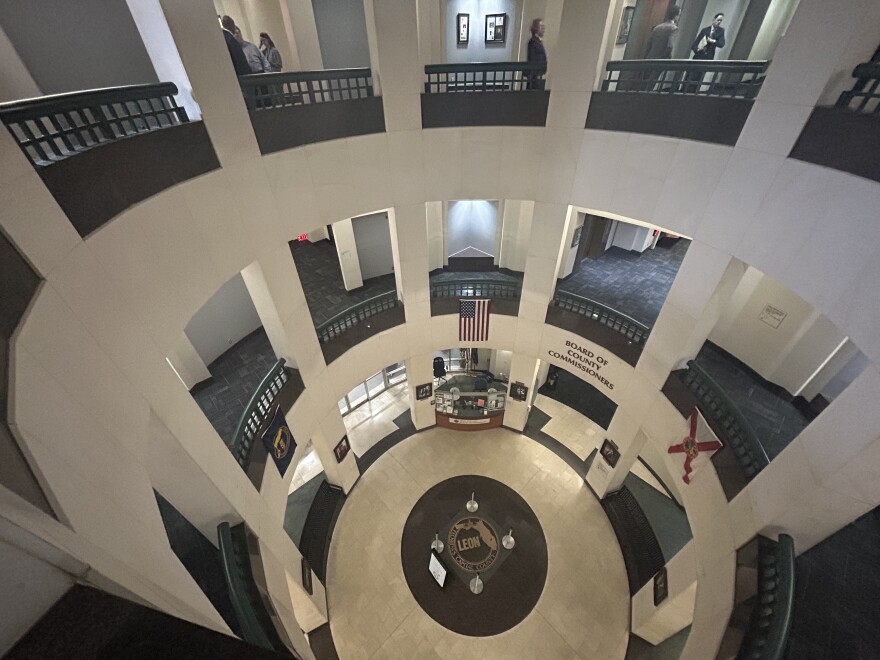 A view looking down through the open rotunda of the Leon County Courthouse in Tallahassee. On the ground floor, the county seal is embedded in the tile floor beneath an American flag hanging from the second level.