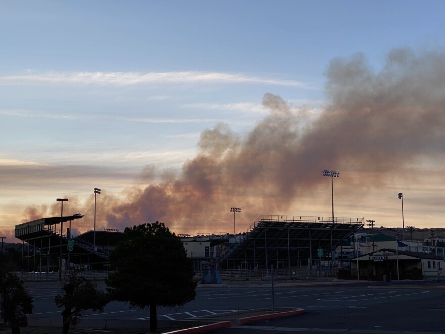 Smoke casts a shadow on a sunset behind a stadium