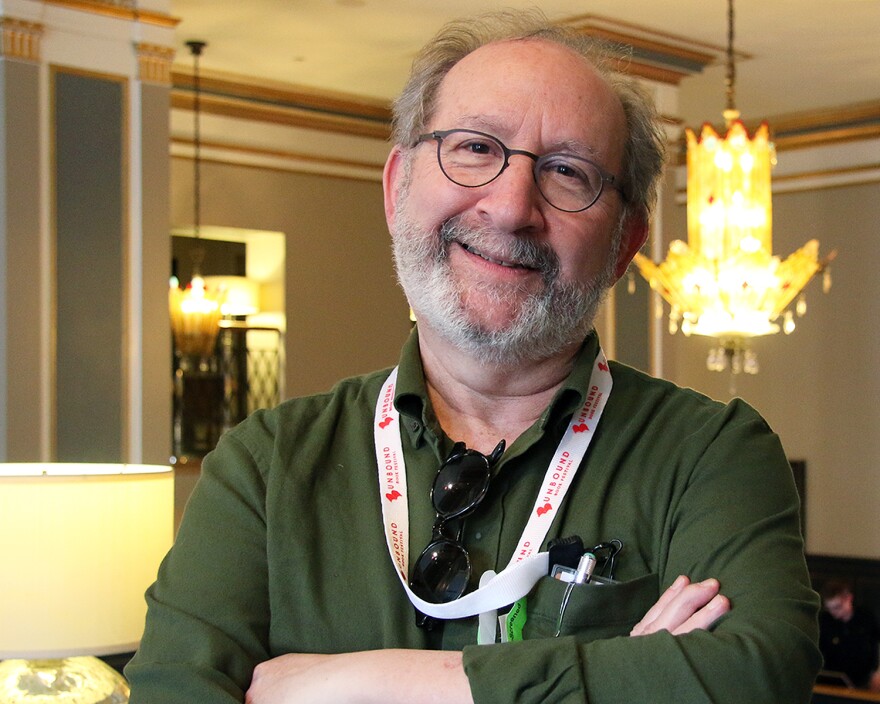 Steve Paul wears glasses and an Unbound Book Festival lanyard around his neck. He's smiling to camera with his arms folded across his chest.