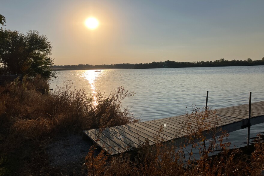 A dock juts out into the water at a lake. A boat is visible in the distance.