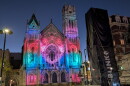 Colored lights cover the facade of a church at dusk.