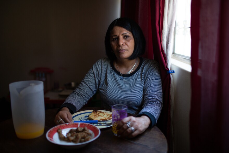 Yroné Camelia Araujo Barreto, a 50-year-old Venezuelan migrant living in Quito, Ecuador, at the dining room table. She is eating a traditional Venezuelan dish of <em>cachapa, </em>round dough made from corn, filled with pork. She typically eats two meals a day if she's lucky enough to afford it.