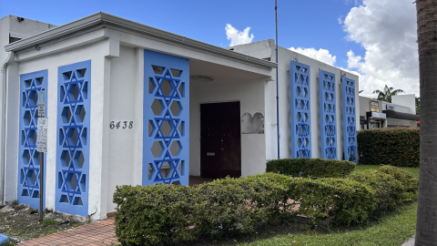 A white building decorated with blue stars of david at the entryways. A shadow is by the front door where a plaque once was.