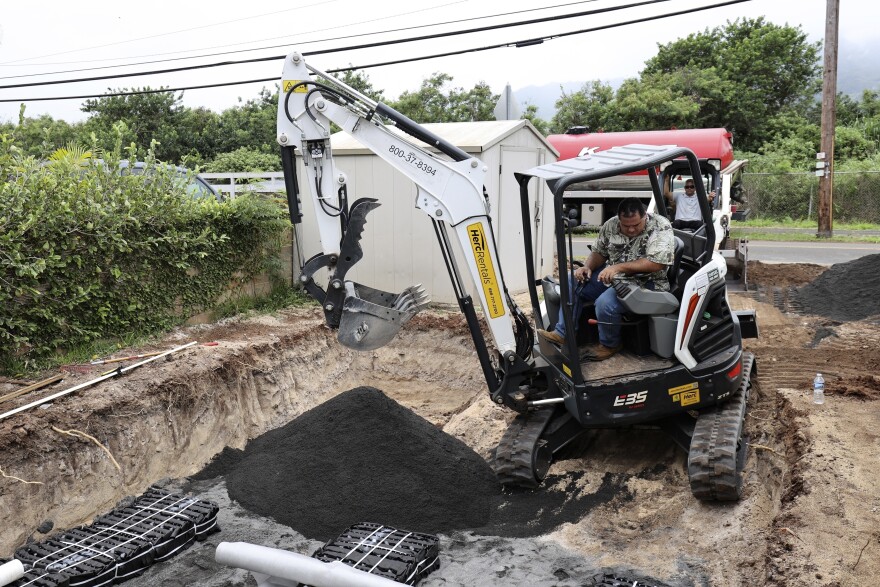 Contractor Wendall Bandmann drives an excavator helping to install a leach field, which is connected to a septic tank, to replace a residential cesspool, May 11, 2023, in Waialua, Hawaiʻi.
