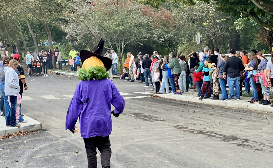 A man in a Jack-O-Lantern costume watches as coffin race competitors line up at the starting line.