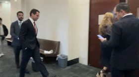 James Fishback, wearing a suit, walks down a courthouse hallway toward a courtroom door, accompanied by others in business attire.