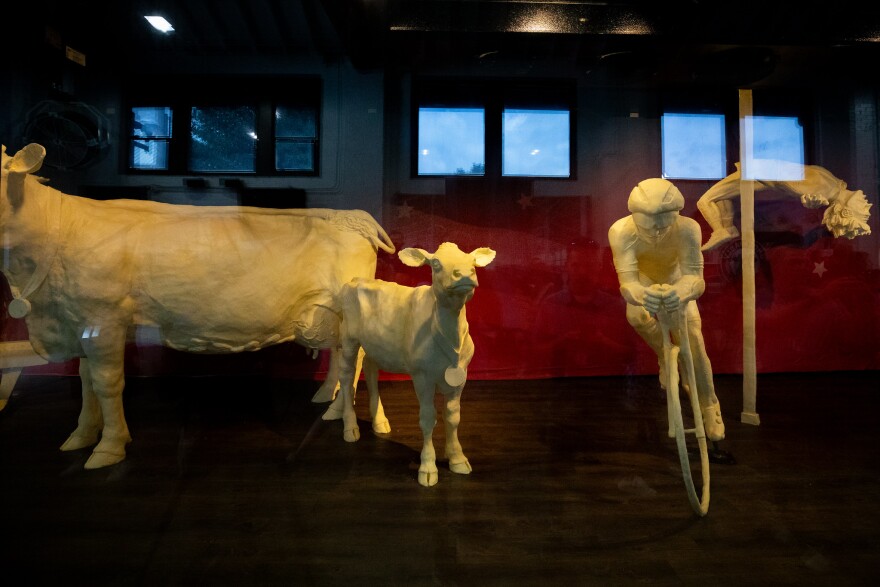 A small yellow calf sculpted out of butter stands next to a butter sculpture of a biker and a gymnast at the Ohio State Fair in 2024.