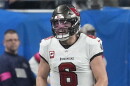 football player with white jerseys and pewter helmet celebrate on the field.