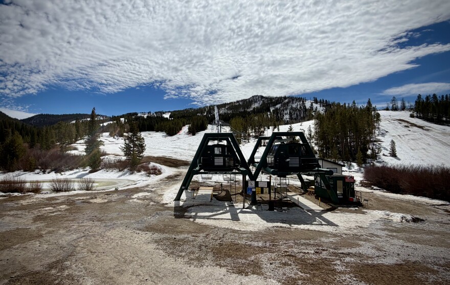 A ski lift surrounded by dirt and some snow further up the mountain on a mostly sunny day.