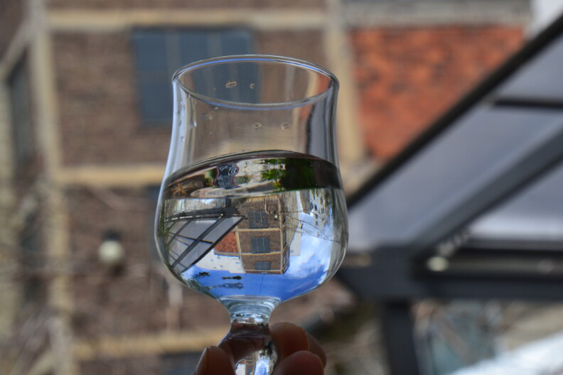 Someone holds a glass of water, which reflects a building.