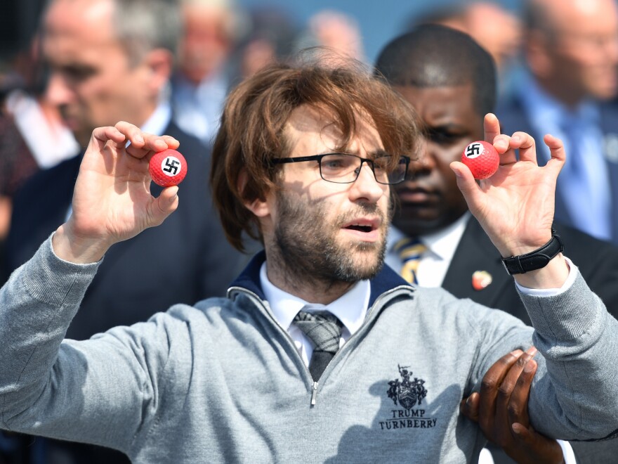 Comedian Lee Nelson is taken away by security Friday while holding golf balls stamped with swastikas, as he protests Donald Trump, at the opening of Trump's resort in Scotland.