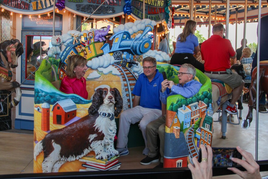 Governor Mike DeWine, right, and his wife, Fran, left, sit on a train-themed bench that includes a carving of their dog, Dolly, on the opening ride of the new carousel at the Ohio State Fairgrounds, July 25, 2026.