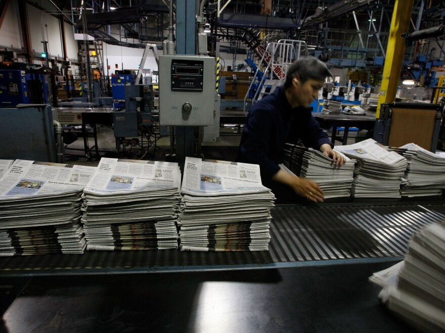 A worker at a <em>San Francisco Chronicle</em> printing plant arranges stacks of freshly printed newspapers in 2007. Its digital version, like that of so many newspapers', is behind a paywall.