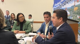 People sit around a table as a man speaks into a microphone.